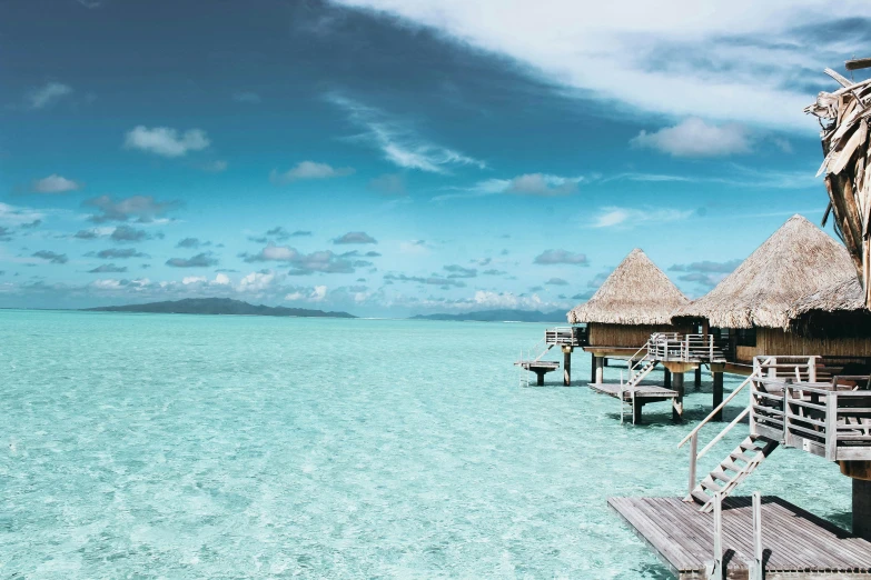 a couple of huts sitting on top of a body of water, by Tom Bonson, trending on unsplash, visual art, crystal clear blue water, moana, arper's bazaar, brochure