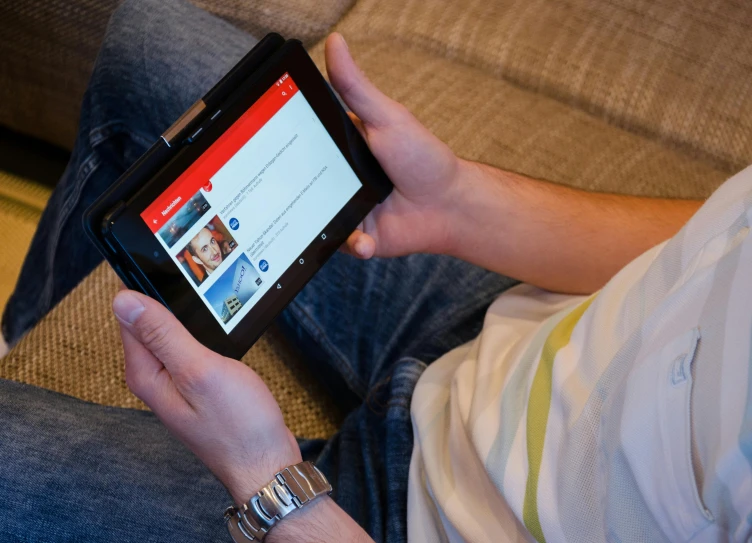 a man sitting on a couch holding a tablet computer, pexels, youtube logo, multiple stories, bottom angle, youtube