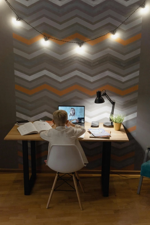 a person sitting at a desk with a laptop, wallpaper on the walls, zig zag, indoor lighting, high angle