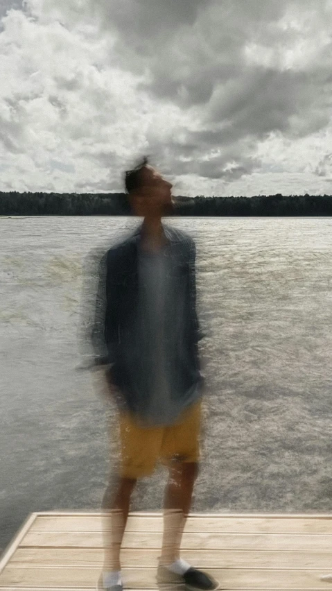 a man standing on a dock next to a body of water, an album cover, by Byron Galvez, video art, blurred face, ignant, looking happy, gif