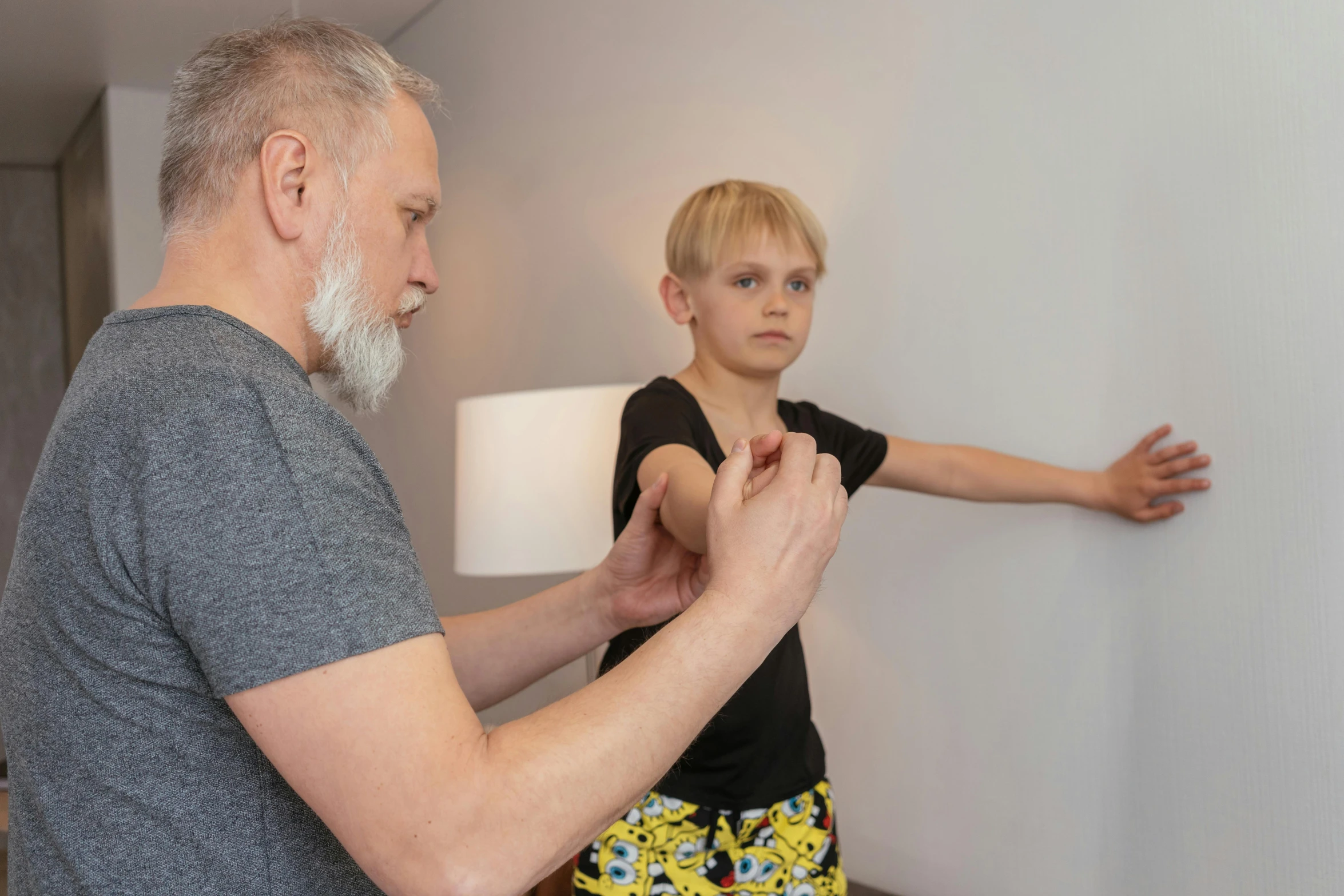 a man standing next to a little boy in a room, scaled arm, profile image, clinical, bend over posture