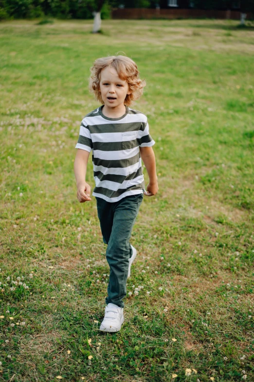 a little boy that is standing in the grass, wearing pants and a t-shirt, walking towards the camera, wearing stripe shirt, premium quality