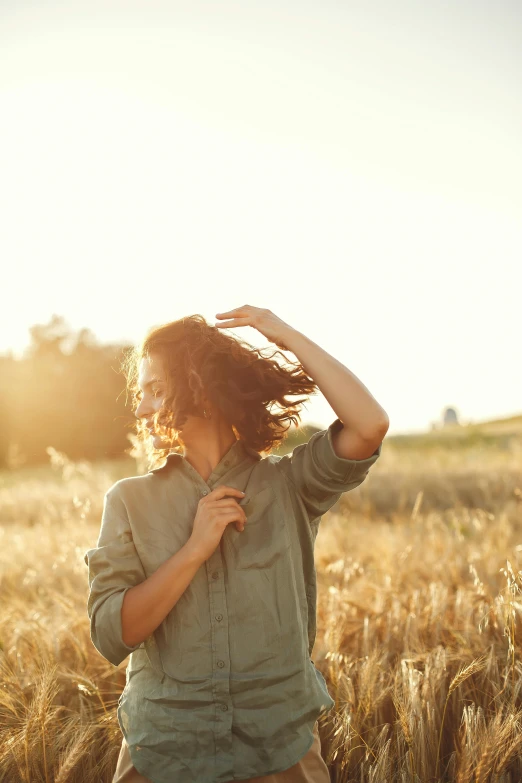 a woman standing in a field of wheat, trending on unsplash, dynamic wavy hair, sun lit, wearing a linen shirt, playful pose