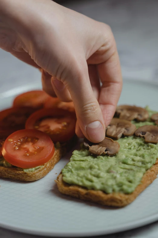 a white plate topped with a sandwich covered in guacamole, by Matthias Stom, pexels, eating a mushroom, timelapse, hand made, also one tomato slice