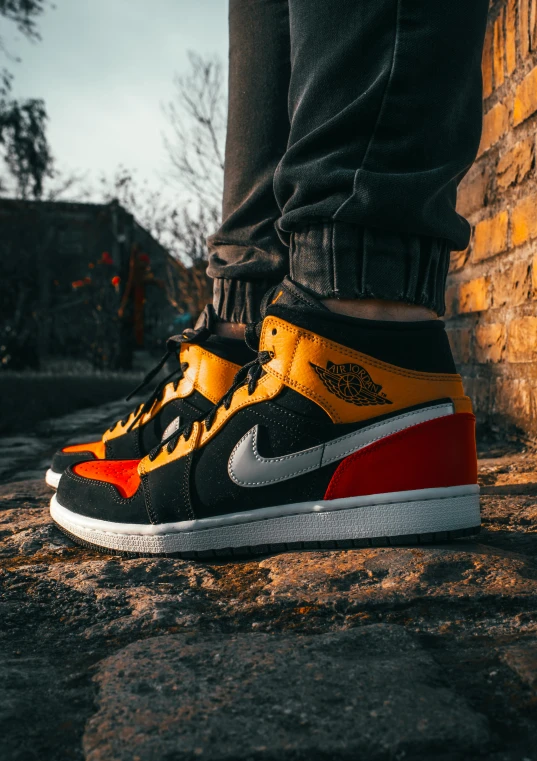 a person standing in front of a brick wall, inspired by Jordan Grimmer, trending on pexels, black and yellow and red scheme, “air jordan 1, orange red black white, sneaker photo