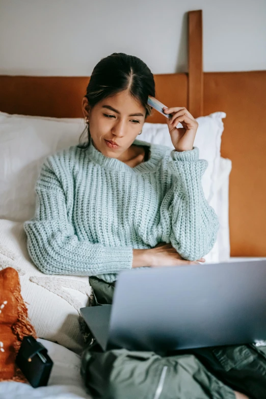 a woman sitting on a bed using a laptop, with teal clothes, stressing out, vietnamese woman, thumbnail