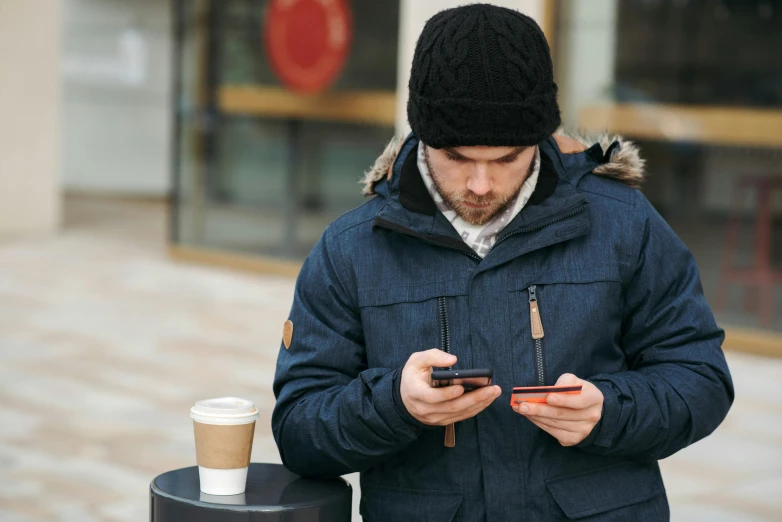 a man is looking at his cell phone, by John Henderson, trending on pexels, knitted hat, avatar image, wearing jacket, greig fraser