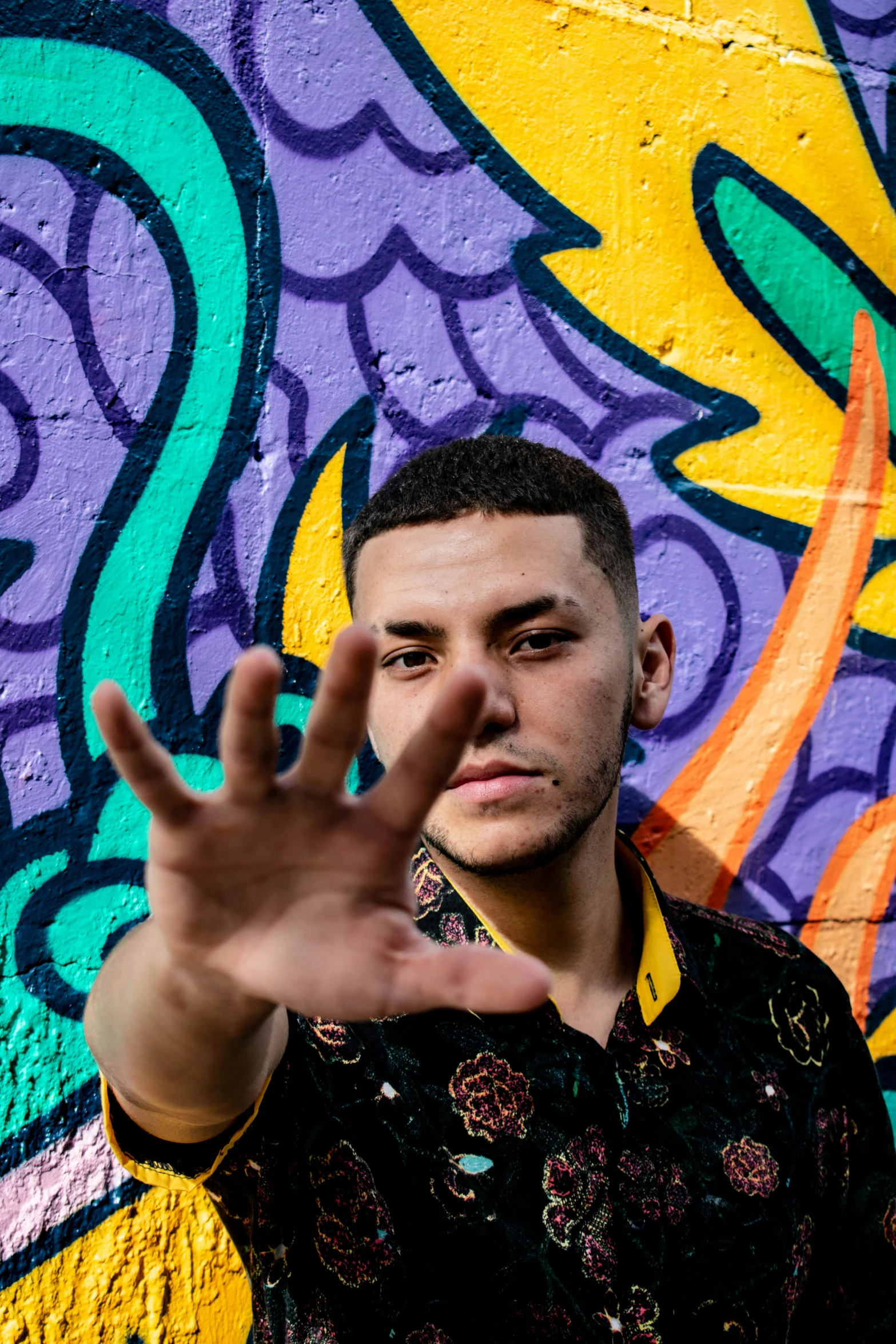 a man standing in front of a wall covered in graffiti, an album cover, inspired by Carlos Berlanga, trending on pexels, hand gesture, non-binary, gal yosef, teddy fresh