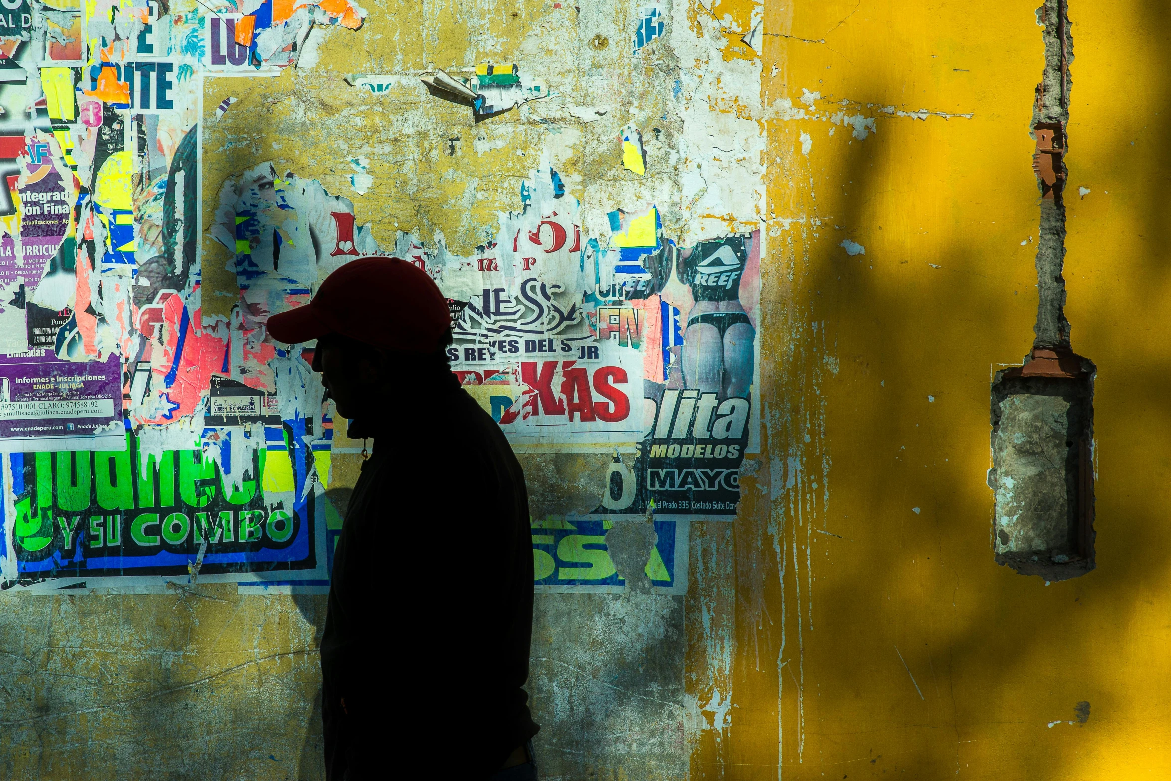 a man standing in front of a wall covered in stickers, a photo, by Tobias Stimmer, pexels contest winner, graffiti, faded red and yelow, back light, cuba, newspaper collage