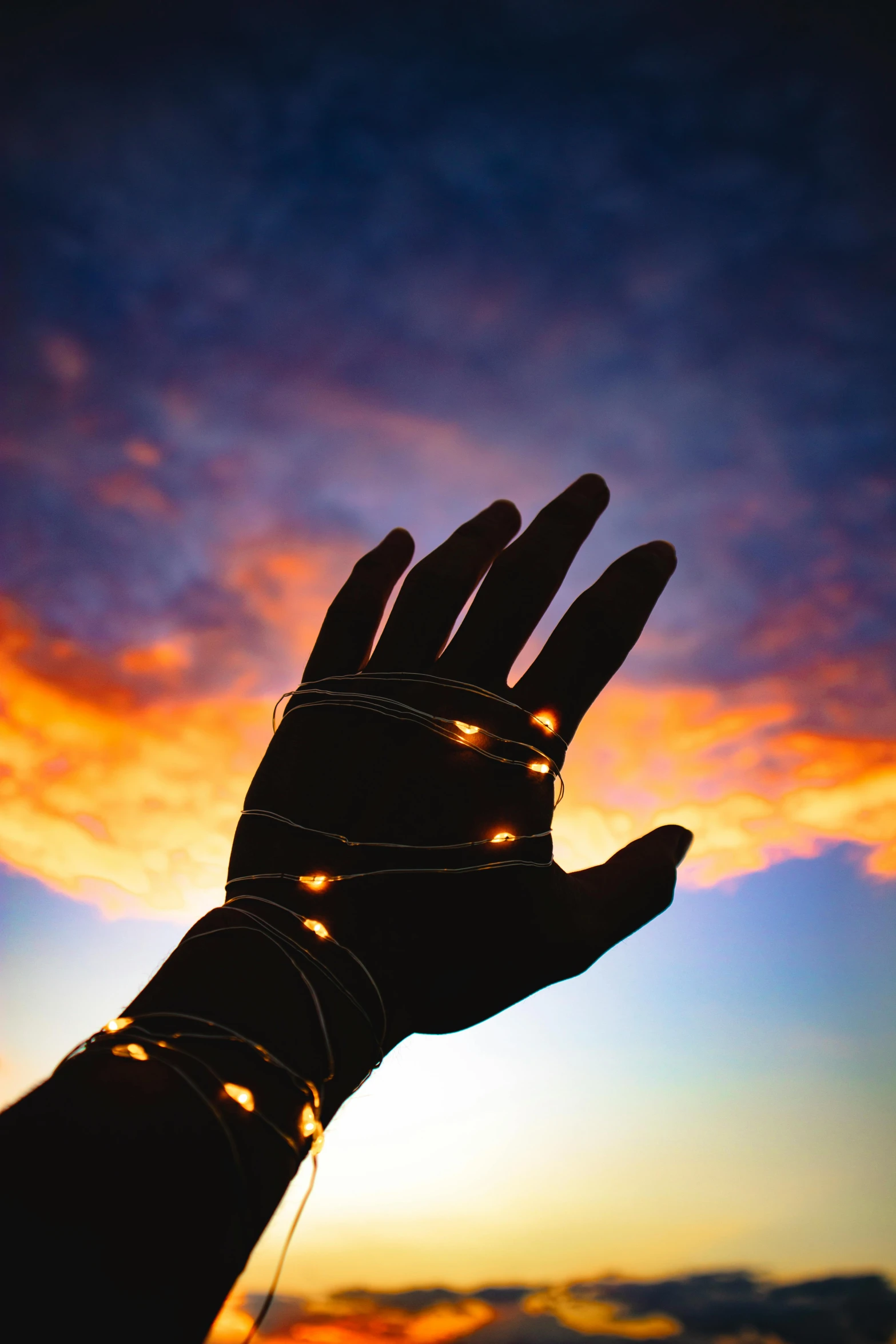 a person holding their hand up in the air, by Dan Content, unsplash, light and space, black and gold wires, binary sunset, healing glowing lights, on a bright day