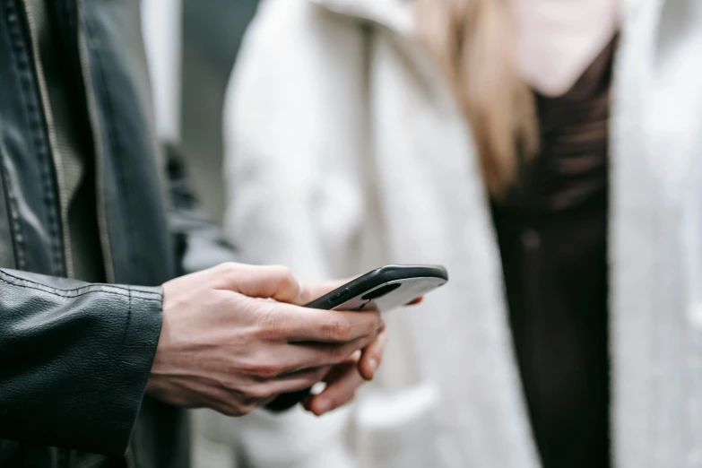 a close up of a person holding a cell phone, trending on pexels, happening, male and female, a man wearing a black jacket, low colour, really long