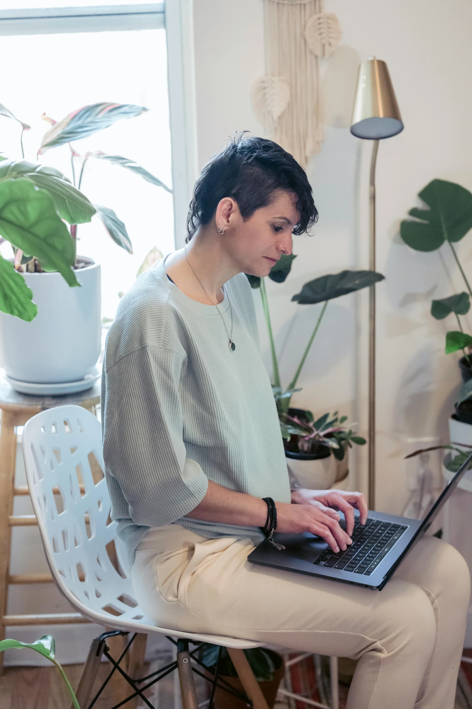 a woman sitting on a chair using a laptop computer, by Carey Morris, trending on unsplash, arbeitsrat für kunst, room full of plants, androgynous male, pastel', centered shot