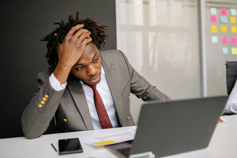 a man sitting at a desk in front of a laptop computer, pexels, renaissance, wearing a worn out suit, black people, coloured, struggling