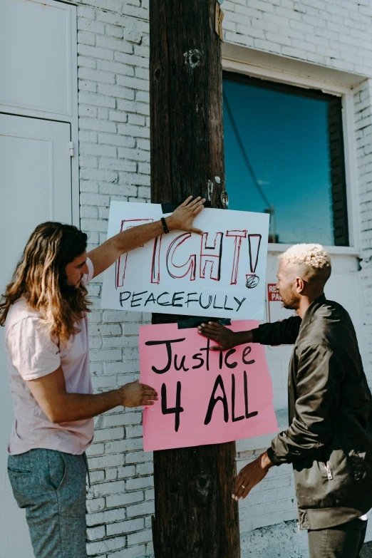 two people hanging signs on a pole in front of a building, by Matt Cavotta, trending on unsplash, fight, peace, instagram picture, justice