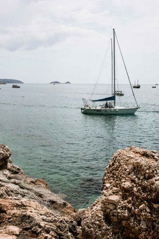 a couple of boats that are in the water, by Carlo Carrà, unsplash, in the distance is a rocky hill, ibiza, sailboat, overcast day