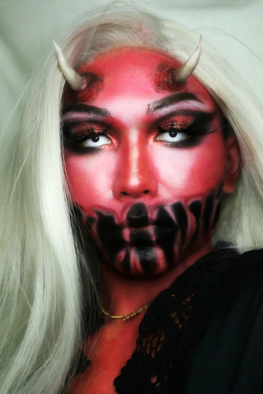 a woman with horns painted on her face, an album cover, reddit, satan in hell, instagram post, red - black, drag