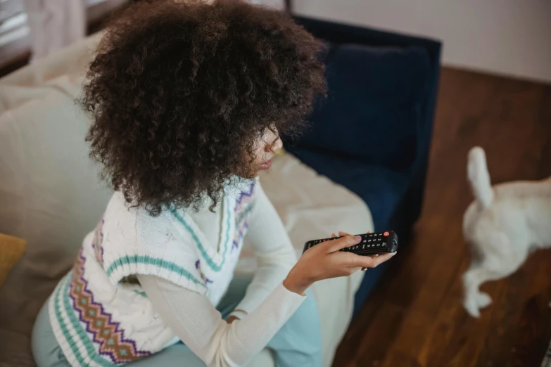 a woman sitting on a couch holding a remote control, pexels, black teenage girl, woman with braided brown hair, with afro, on a canva