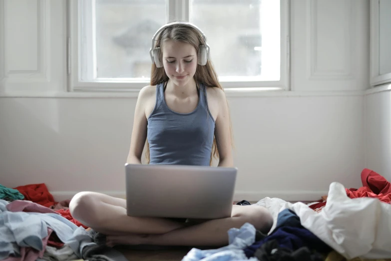 a woman sitting on the floor in front of a laptop, girl wearing headphones, wearing a crop top, in small room, with clothes on