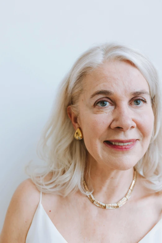 a woman standing in front of a white wall, a character portrait, by Maggie Hamilton, trending on unsplash, white-hair pretty face, pearl earring, neck wrinkles, smooth golden skin