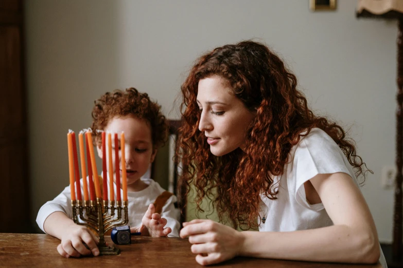 a woman and a child sitting at a table with a menorah, pexels, brown curly hair, a wooden, led, 1 2 9 7