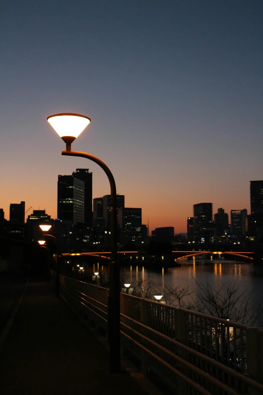 a street light sitting next to a body of water, inspired by Kanō Shōsenin, happening, twilight skyline, arasaka, beside the river