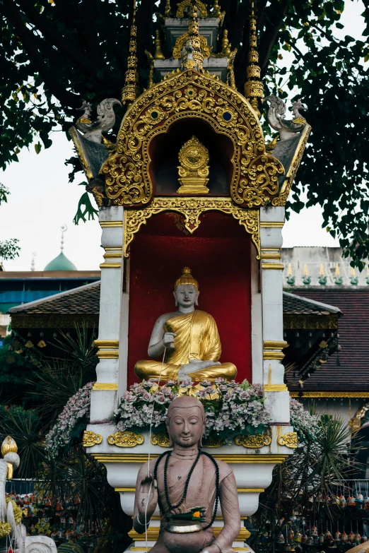 a statue of a man sitting in front of a building, pagoda, gold decorations, maroon, lush surroundings