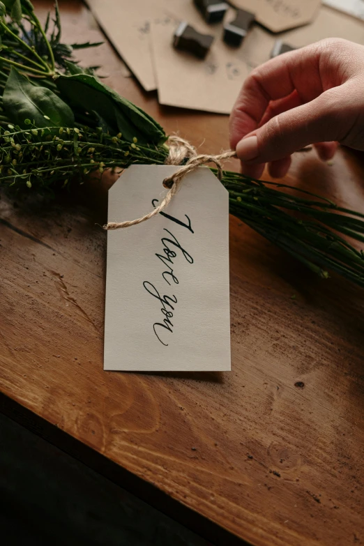 a person holding a piece of paper with writing on it, by Grace English, pexels contest winner, herbs hanging, floral design, tag, owen gent