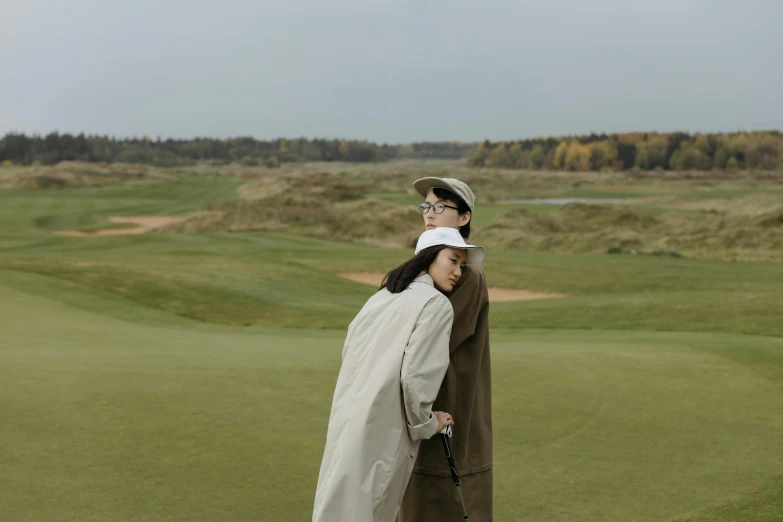 a man and woman standing next to each other on a golf course, by Emma Andijewska, unsplash, visual art, trench coat, kim hyun joo, thumbnail, baggy clothing and hat