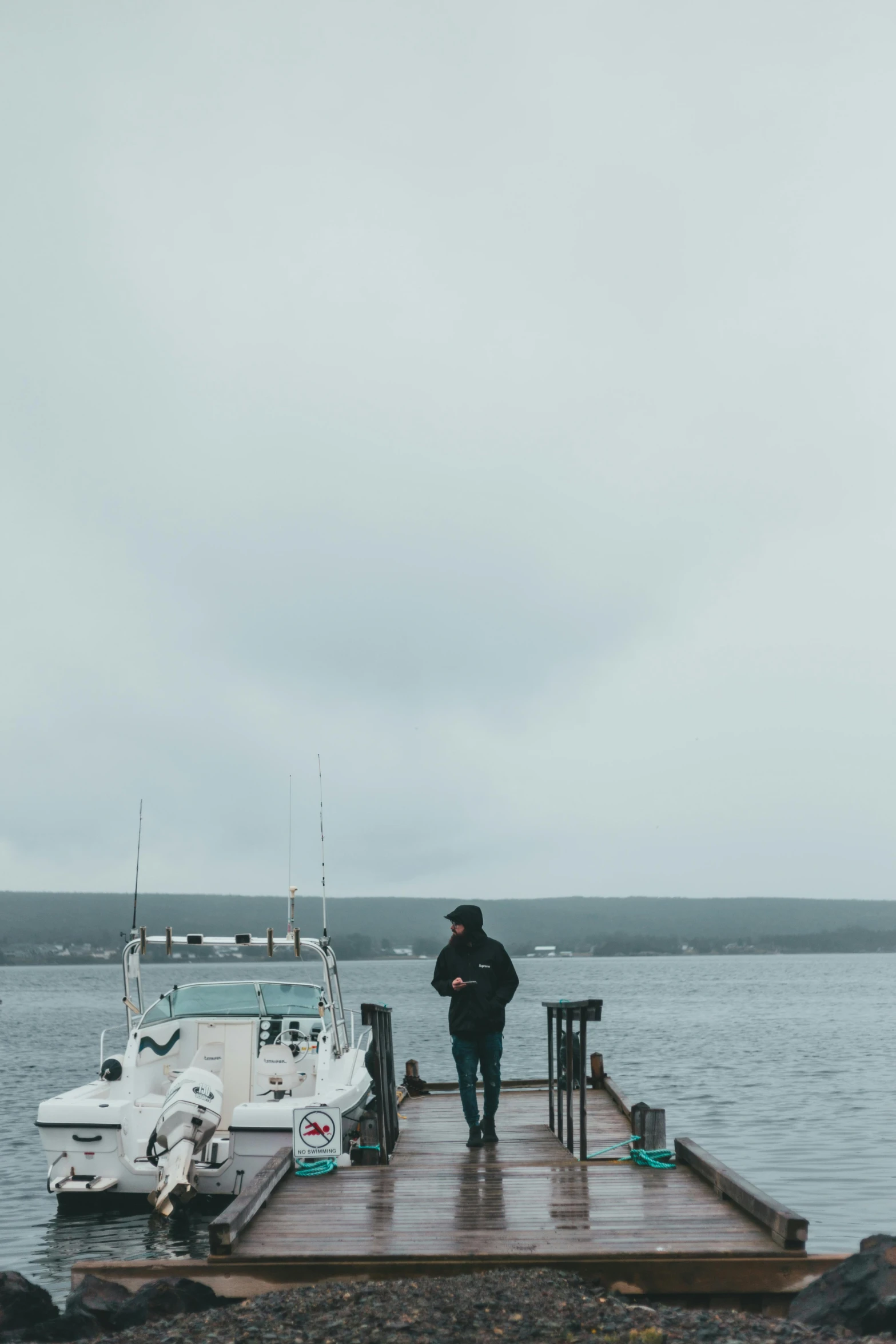 a man standing on a dock next to a boat, happening, overcast gray skies, cinematic shot ar 9:16 -n 6 -g, big island, trending on vsco