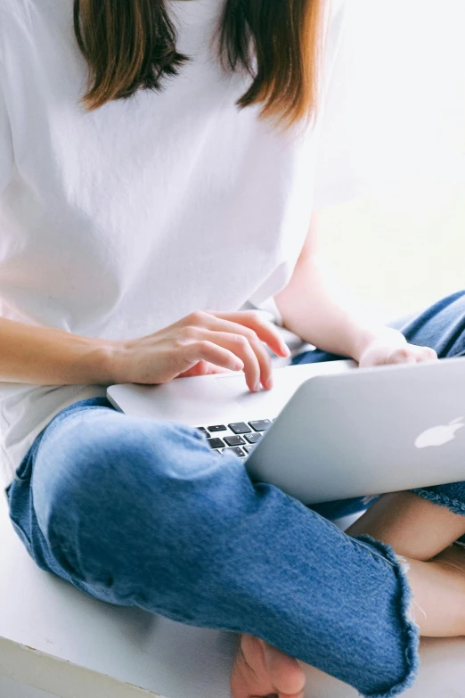 a woman sitting on a window sill using a laptop, by Carey Morris, pexels, white shirt and blue jeans, with apple, pastel', loosely cropped