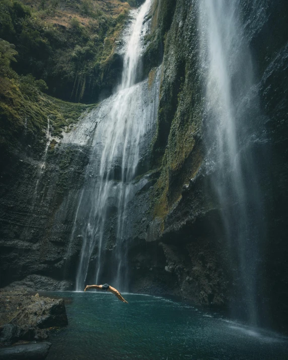 a person swimming in a body of water near a waterfall, by Daren Bader, pexels contest winner, sumatraism, soaring, slightly tanned, swinging on a vine over a chasm, trending on vsco