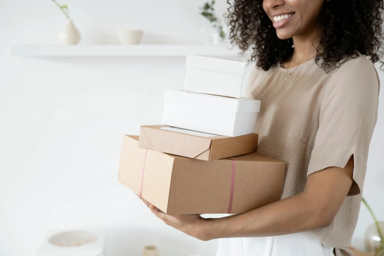 a woman holding a stack of boxes in her hands, by Eden Box, private press, white, gifts, pack, diverse