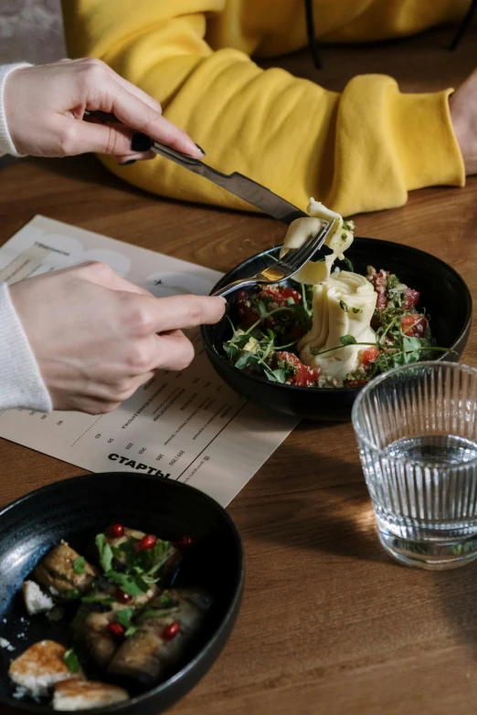 a couple of people sitting at a table with plates of food, by Adam Marczyński, unsplash, cutting a salad, detail shot, dumplings on a plate, sleek hands