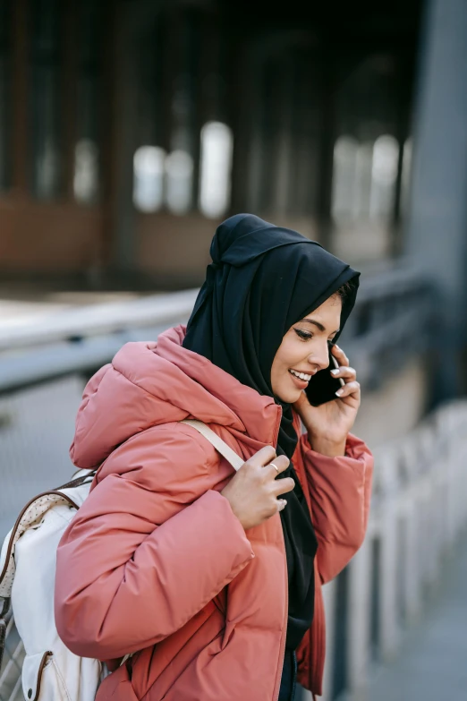 a woman in a pink jacket talking on a cell phone, inspired by Modest Urgell, trending on pexels, hurufiyya, wrapped in a black scarf, malaysian, her friend, swedish