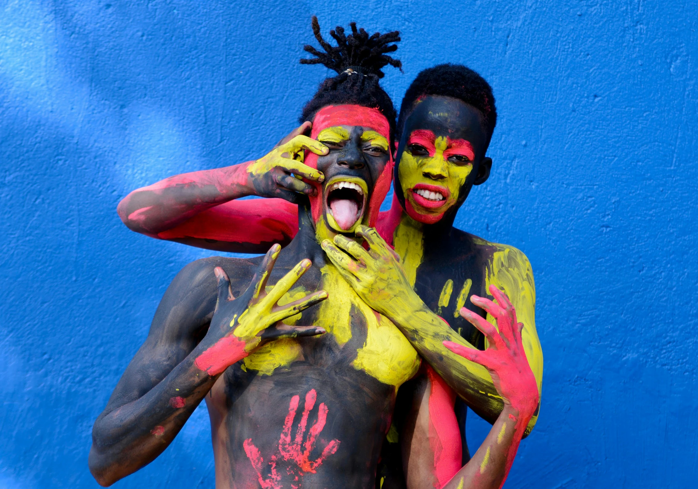 a couple of men standing next to each other, pexels contest winner, black arts movement, bodypaint, red yellow blue, triumphant pose, black teenage boy