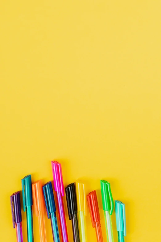 a group of pens sitting on top of a yellow surface, by Robbie Trevino, pexels, crayon art, colored neons, schools, no - text no - logo, instagram photo