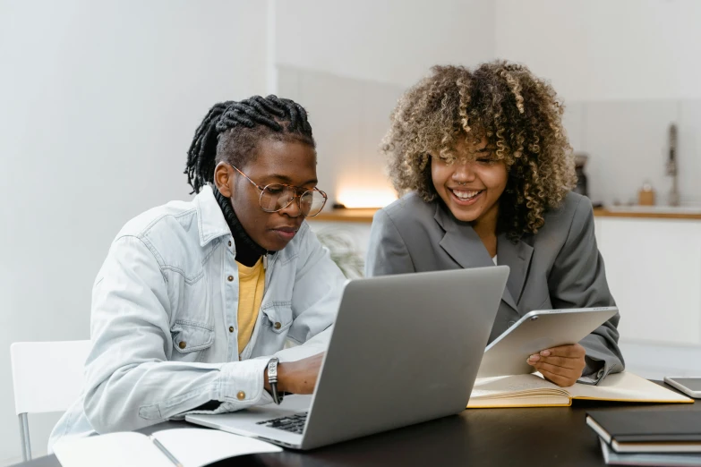 two women sitting at a table looking at a laptop, trending on pexels, school class, avatar image, black people, background image