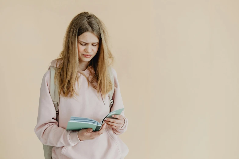 a woman sitting on a chair reading a book, trending on pexels, happening, wearing a pastel pink hoodie, girl wearing uniform, girl standing, beige hoodie