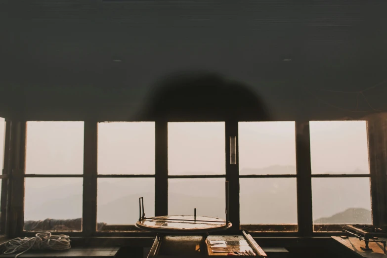 a boat sitting on top of a table in front of a window, a picture, unsplash contest winner, light and space, lookout tower, sitting on a mocha-colored table, hazy, pictured from the shoulders up