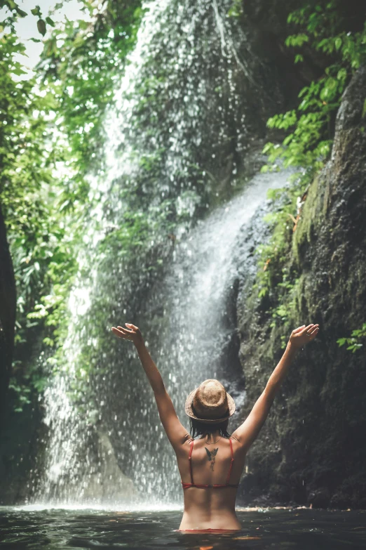a woman standing in the water in front of a waterfall, happy vibes, hanging from a tree, waving, jungle