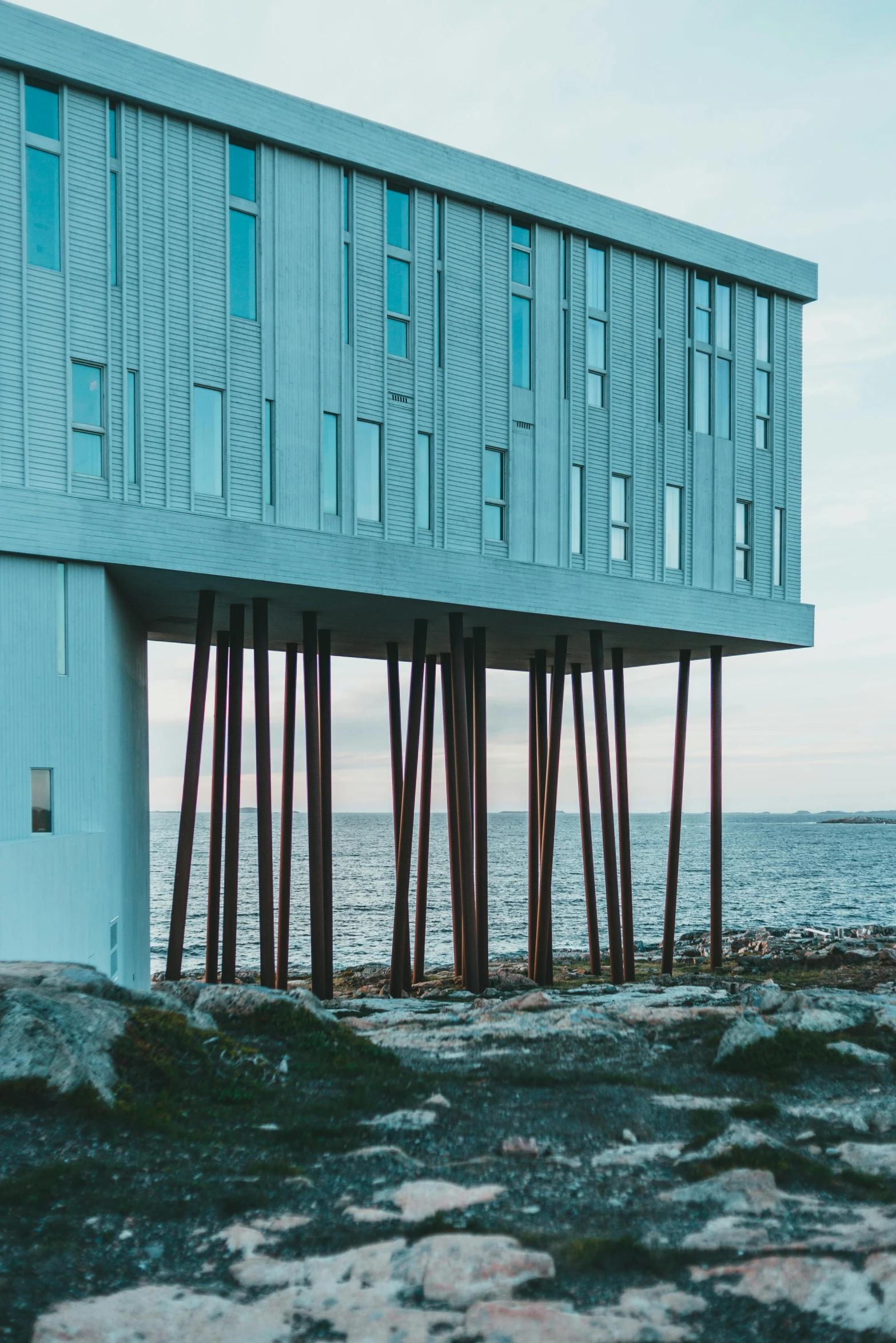 a building sitting on top of a rock next to the ocean, inspired by Wilhelm Marstrand, pexels contest winner, modernism, tall columns, aquamarine windows, subsurface scandering, houses on stilts