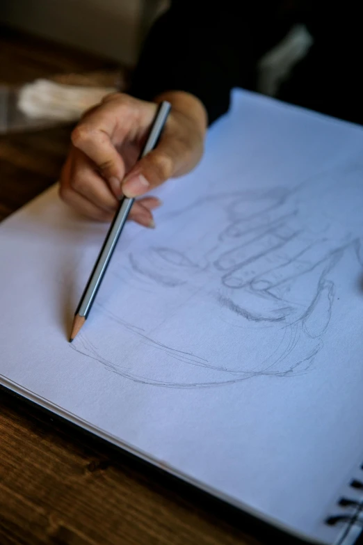 a person drawing on a piece of paper with a pencil, a drawing, by Dóra Keresztes, pexels contest winner, process art, back of hand on the table, caricaturist, anatomical drawing, drawing pictures on a notebook