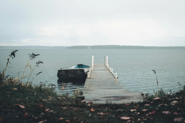 a boat sitting on top of a lake next to a dock, inspired by Elsa Bleda, pexels contest winner, grey skies, cottage core, grey, lake blue