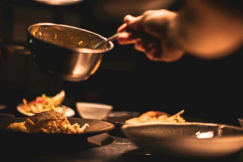 a person pouring food into a bowl on a table, by Daniel Lieske, pexels contest winner, renaissance, nightlife, crisp details, chefs table, pan and plates