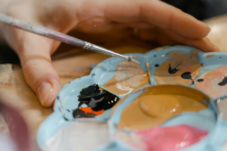 a close up of a person holding a paint brush, by Julia Pishtar, trending on pexels, process art, emma bridgewater and paperchase, hand built ceramics, lightblue acrylic paintdrip tar, face painting