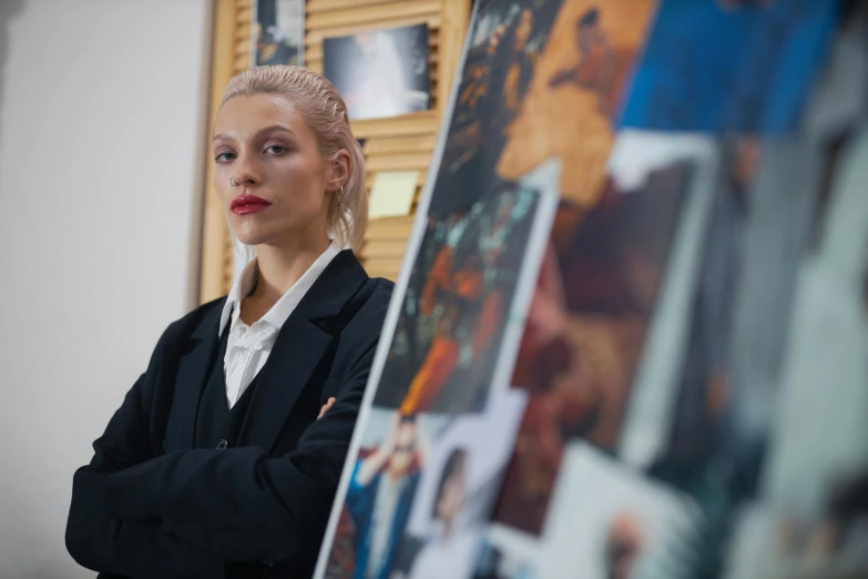 a woman standing in front of a bunch of pictures, a photorealistic painting, unsplash, academic art, wearing a black suit, like a professional model, eleven/millie bobbie brown, artem chebokha