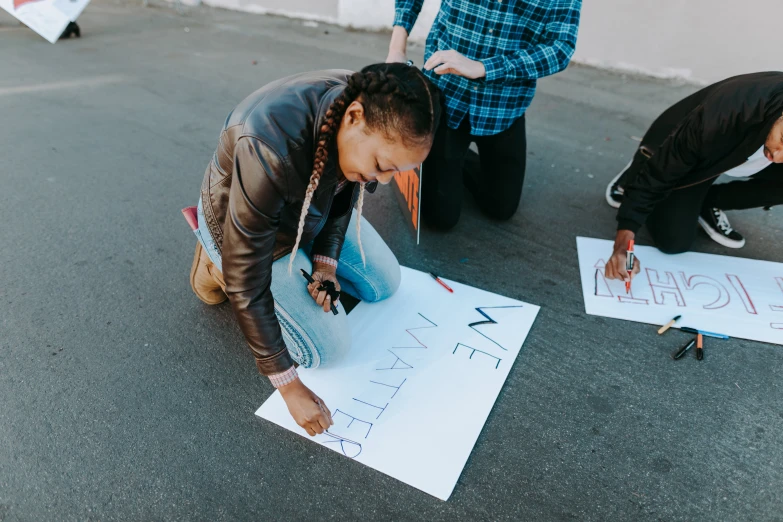 a group of people drawing on a piece of paper, a photo, by Julia Pishtar, pexels contest winner, graffiti, woman holding sign, on ground, promotional image, protest