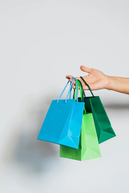 a person holding several shopping bags in their hand, by Matthias Stom, trending on unsplash, green and blue, square, on a gray background, holiday