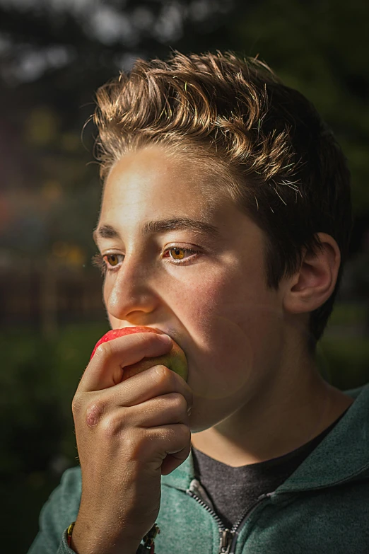 a young man eating an apple in a park, by Michael Goldberg, pexels, hyperrealism, portrait of 14 years old boy, backlit portrait, diana levin, color portrait