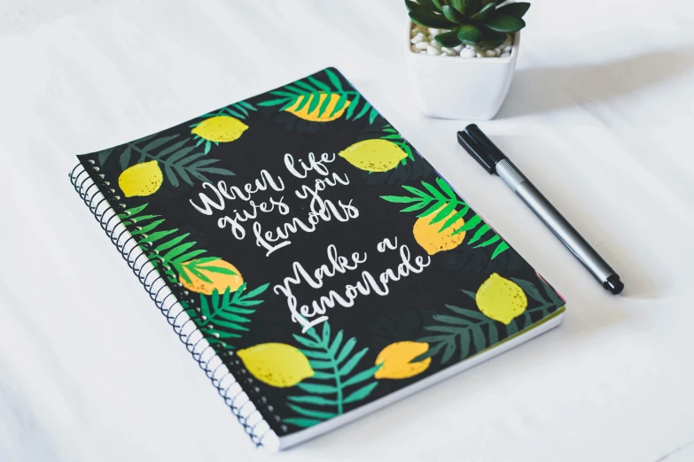 a notebook sitting on top of a table next to a potted plant, lemons, trendy typography, full product shot, round
